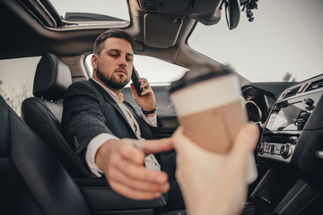 Handsome caucasian businessman driver inside in vehicle  with coffee and gadget and check mail and talking with partners