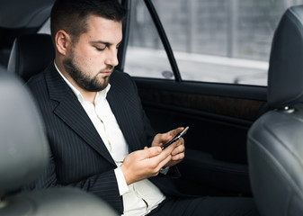 Handsome caucasian businessman driver inside in vehicle  with coffee and gadget and check mail and talking with partners