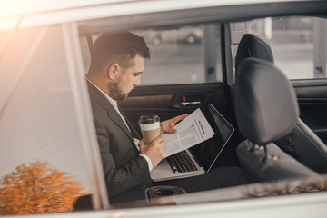 Handsome caucasian businessman driver inside in vehicle  with coffee and gadget and check mail and talking with partners