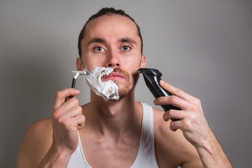 Man shaving face with various razors on gray background