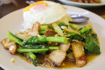 Stir fry Kai Land and Crispy Pork Belly with rice and topping with  fried egg on white plate. Thai food is delicious