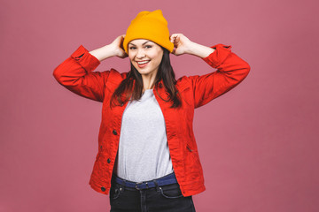Portrait of happy hipster girl in yellow hat and red shirt isolated over pink background.