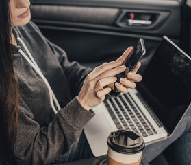 Young pretty woman with smartphone and cup of coffee sit in car