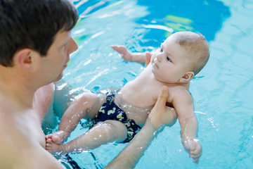 Fototapeta na wymiar Happy middle-aged father swimming with cute adorable baby in swimming pool.