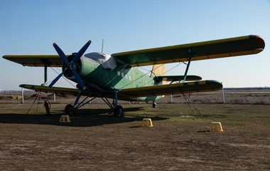 Fototapeta premium Old airplanes. Green and blue corncob. Sports plane of the 19th century. Until now they fly. Touch the antiquity. Propeller and wings. Airplane repair. Aerodrome. Blue sky. Sunny.