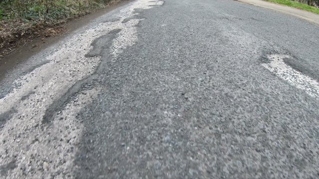 Vehicle driving over a bumpy, damaged road covered in Potholes in the street. 