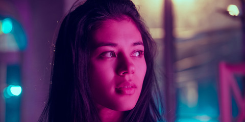Cinematic close up portrait of stylish woman in neon lighted interior. Toned like cinema effects in purple-blue. Caucasian female model looks calm and delighted in colorful lights indoors. Flyer.