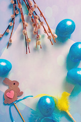 Happy Easter day. Easter composition of blue easter eggs s, pussy-willow branches, green flowers, ribbon, easter bunny. Top view, save space, bokeh effect, Vertical background