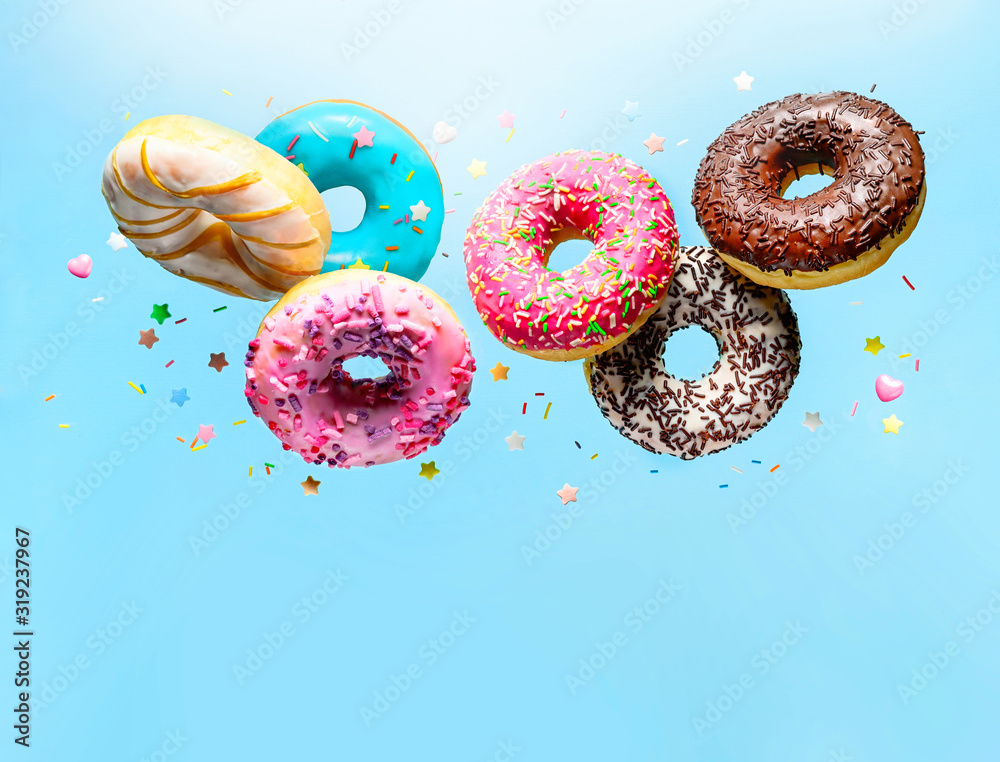 Wall mural flying delicious donuts with sprinkel on blue background with copy space