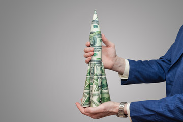 Man holds rocket of paper dollars on isolated gray background.