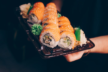 Close-up Hand Waiter holding Set Delicious fresh Sushi slate plate, Japanese raw fish   in traditional restaurant. Philadelphia flesh Rolls served on plate in sushi bar. Copy Space Japan menu service