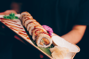 Close-up Hand Waiter holding Set Delicious fresh Sushi slate plate, Japanese raw fish   in traditional restaurant. Philadelphia flesh Rolls served on plate in sushi bar. Copy Space Japan menu service