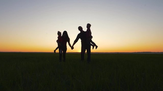 Young happy family walks outdoors at sunset. Silhouette of parents with children.