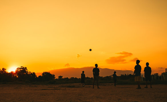 Silhouette action sport outdoors of kids having fun playing soccer football for exercise in community rural area under the twilight sunset. Picture with copy space.
