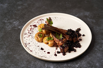 Lamb ribs with baked potatoes on a white plate, close-up.