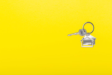 House keys with trinket on color background, top view with copy space. House key on yellow background. Minimal flat lay style with place for text.