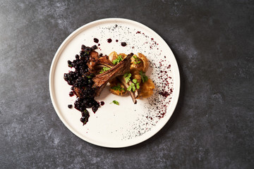 Lamb ribs with baked potatoes on a white plate, close-up.