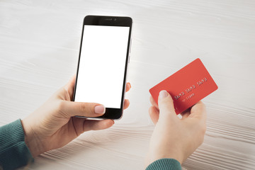 Woman hands holding smartphone with blank screen and red credit card: concept of online banking, online trading, e-commerce