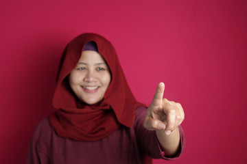 Muslim Woman Smiling and Pointing or Touching Virtual Screen on Red Background With Copy Space