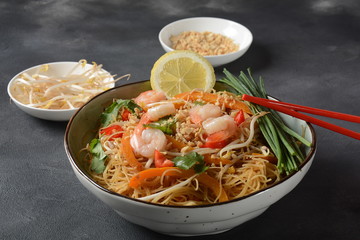 Pad Thai- traditional Thai dish with stir fried rice noodles, shrimps and vegetables on a dark background, copy space