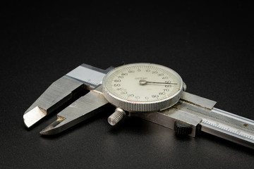 A dial caliper lying on a black background