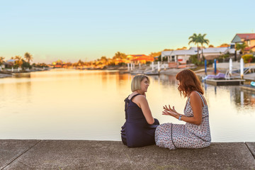 Two women are sitting on a river pier and discussing.