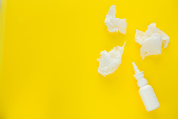 Nasal spray and used paper handkerchiefs on yellow background with copy space. Cold or allergy cure concept. Flat lay.