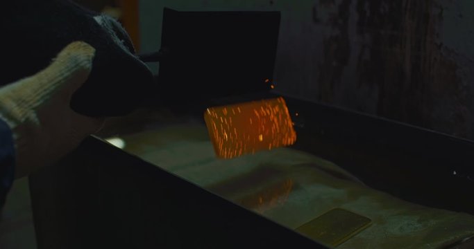 Factory Worker Uses Metallic Tongs to Drop Hot Red Smooth Gold Bar Into Water, Splashes, Black Background, Production