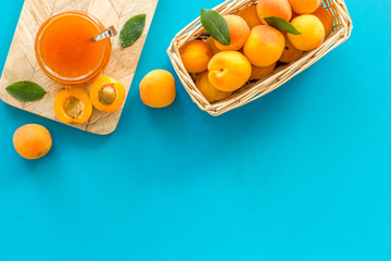 Summer preserves. Apricot jam in jar near fresh fruits on blue background top view frame space for text