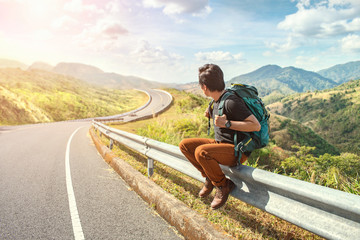 Young man sitting on the roadside. Travel and Holiday concepts. Backpacker on road. Travel man hitchhiking
