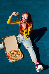 Bright exciting girl with red hair, style of the 90s, 2000s, jacket, wide jeans, bananas, sneakers. Eats pizza out of the box on a basketball court in summer