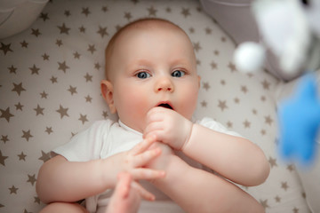 baby boy 5 months old in a white bodysuit lying in a crib top view,textiles for children's room
