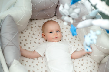 baby boy 5 months old in a white bodysuit lying in a crib top view,textiles for children's room