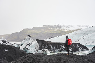 Tourist with red backpack exploring Solheimajokull  glacier (region of Sudurland, Iceland)