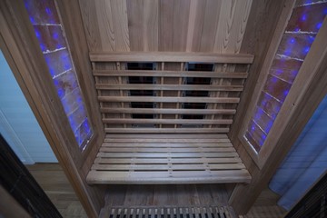 Infrared sauna interior close up view. Wooden walls and bench, ceramic heaters. Healthy lifestyle concept.