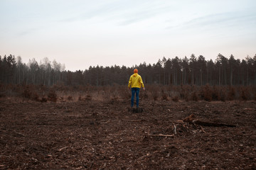 Man weared in yellow raincoat observes destroyed forest after technological disaster