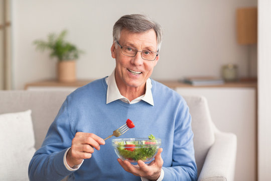 Senior Man Enjoying Salad Sitting On Sofa At Home