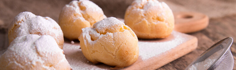Banner of Profiteroles with icing sugar on wooden background. Rustic style. Close up.