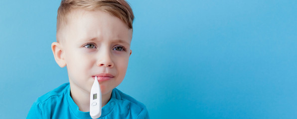 Ill young child with a thermomether, measuring the height of his fever and looking into the camera