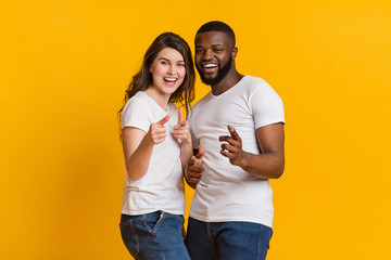 Joyful interracial lovers indiciting fingers at camera and laughing