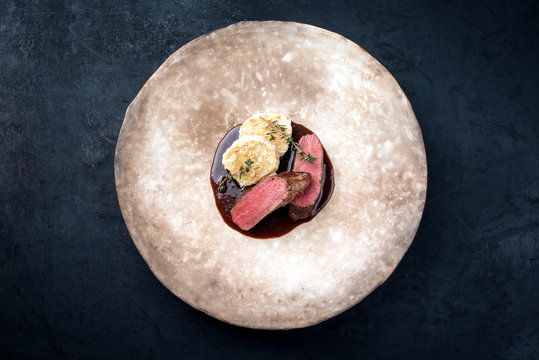 Gebratene dry aged Hirsch Filet Medaillon Steaks natur mit Semelkn&ouml;del und w&uuml;rziger brauner Bratensauce als Draufsicht auf einem Modern Design Teller mit Textfreiraum