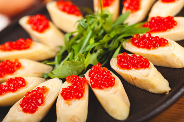 Rolled crepes (pancakes, blini) with red caviar served with arugula on black plate.