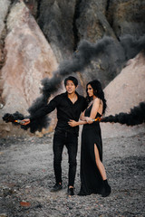 An Asian couple in love lit black smoke bombs in the mountains. Colored smoke