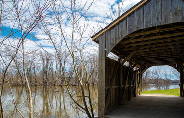 rustic wooden covered bridge by river in spring time