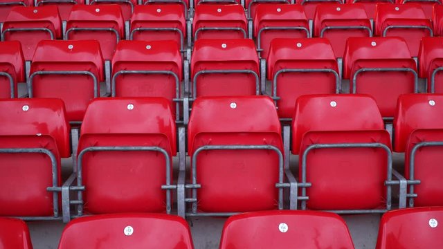 Empty plastic seats in the stadium. The chairs are red with no spectators there.