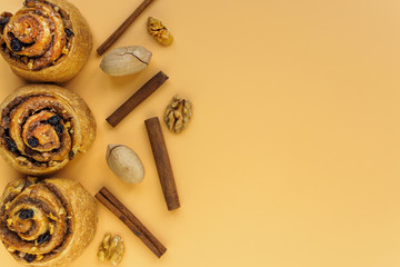 Cinnamon and raisin buns, pecans and walnuts on orange background with copy space