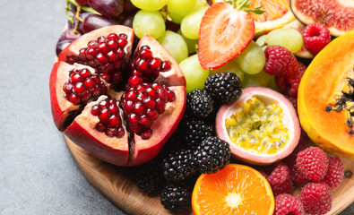 Delicious fruit platter pomegranate papaya oranges passion fruits berries on wooden board on light...