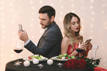 Bored Couple Using Smartphones Sitting Back To Back On Romantic Date
