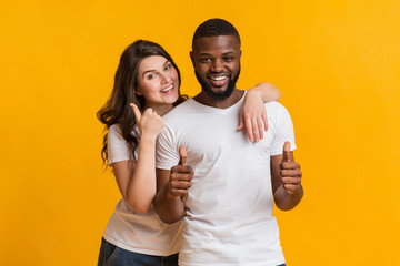 Happy millennial couple embracing and gesturing thumbs up at camera