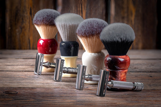 Metallic safety razors and shaving brushes on rustic wooden boards background, barber shop concept